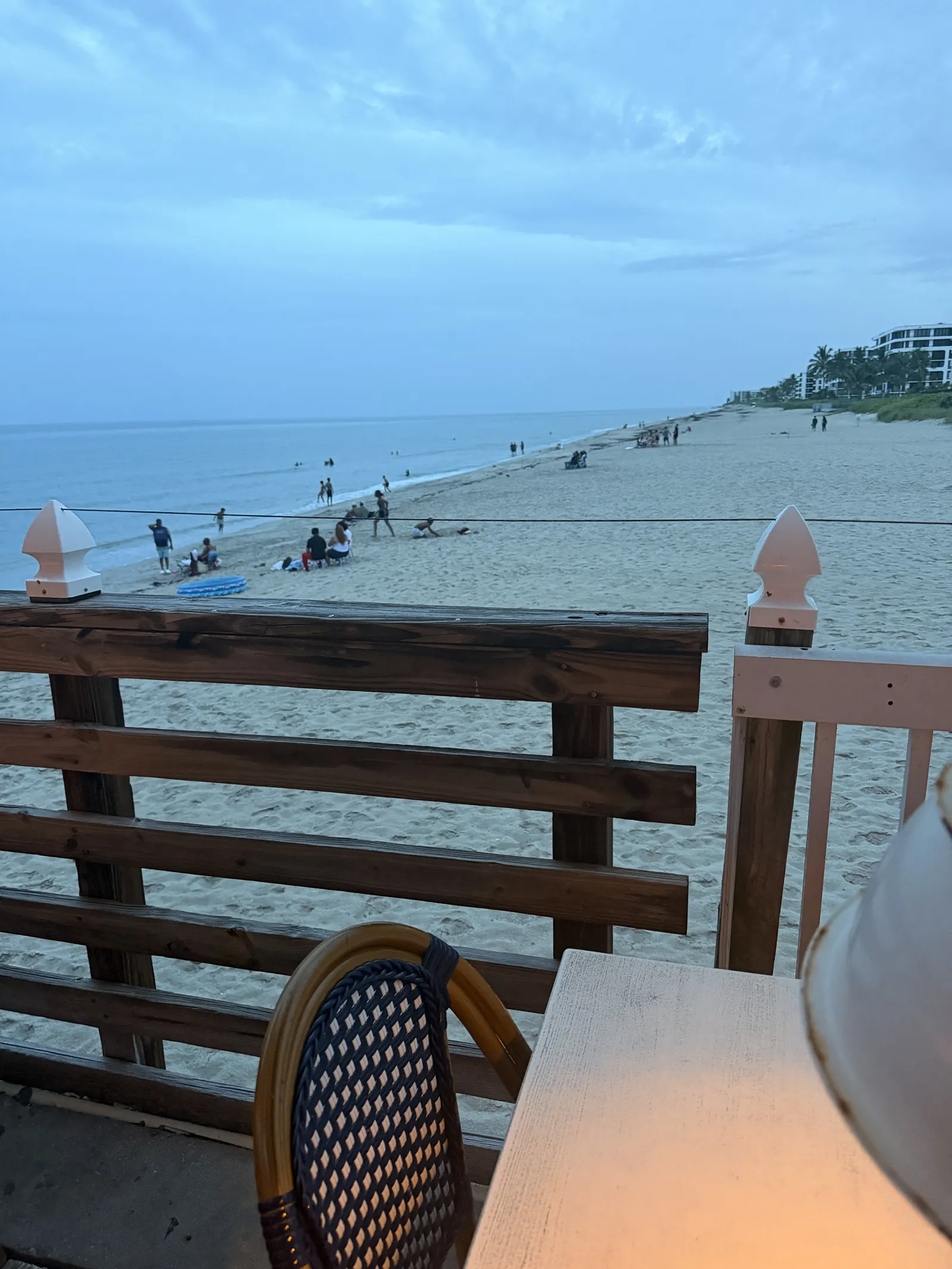 The beach seen over the railing at Benny's near sunset, walkers along the shoreline