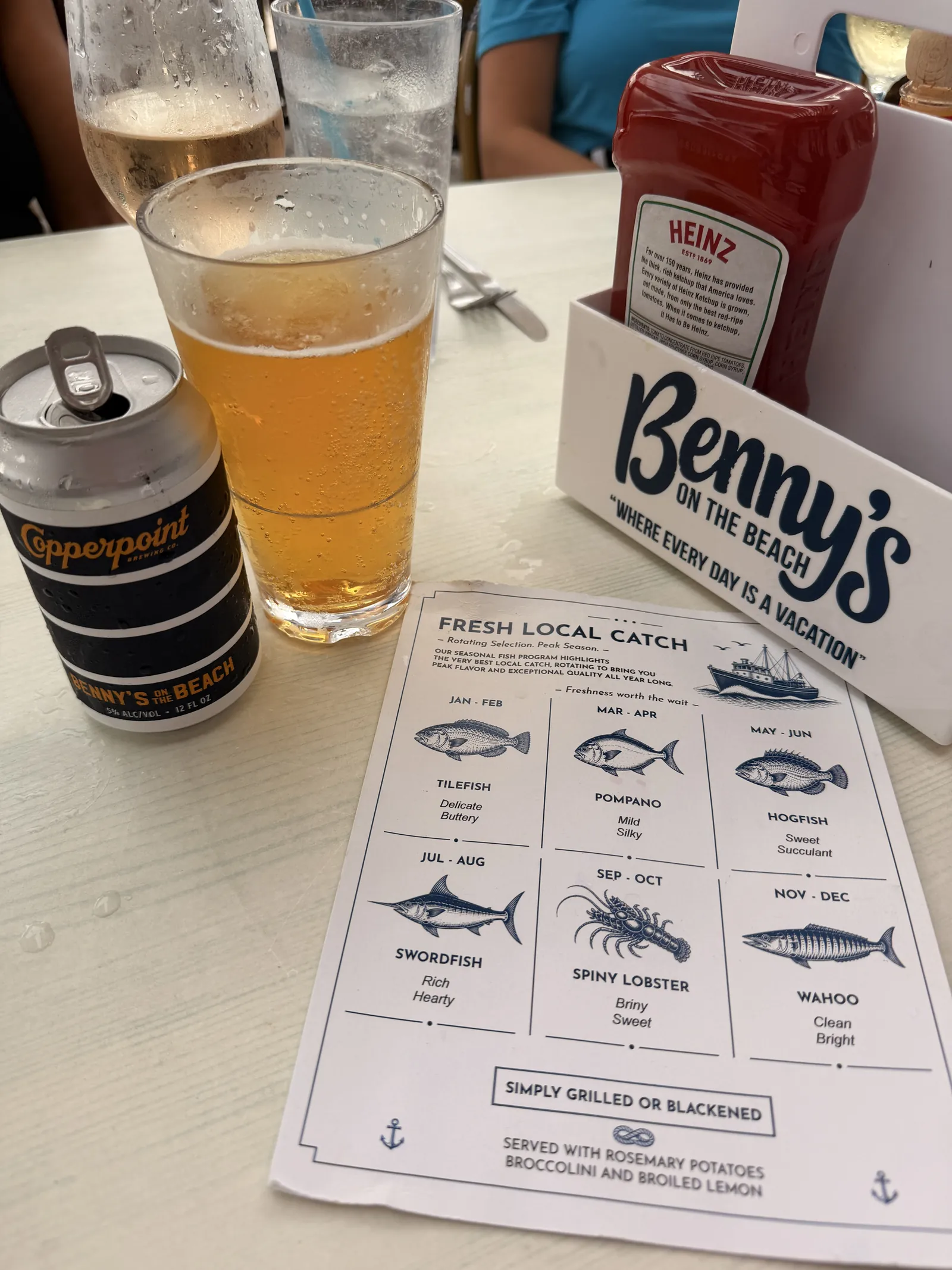 A beer and Benny's menu listing the fresh local fish by month, ketchup on the table