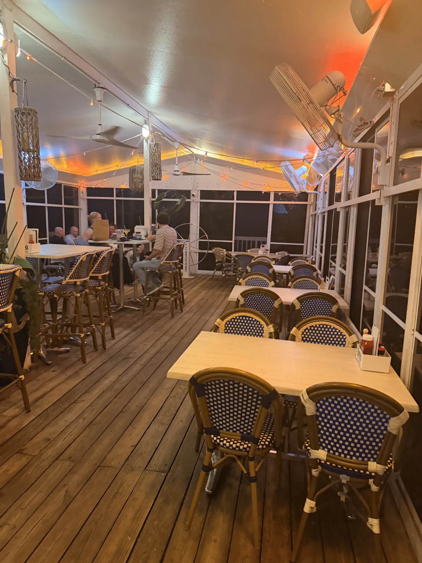The covered deck at Benny's at night, empty tables in front and string lights overhead