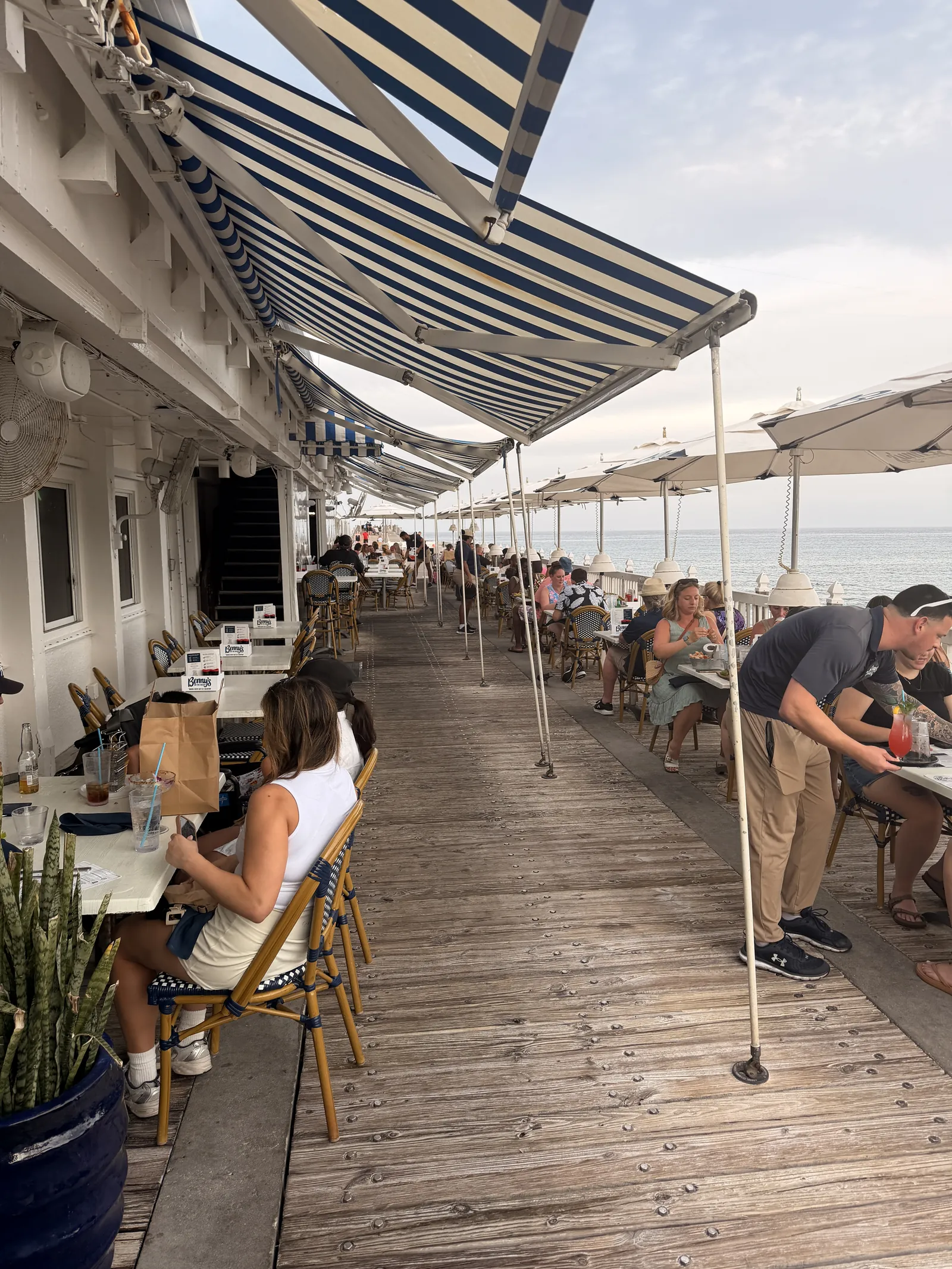 Diners under the blue and white striped awnings at Benny's, a server bringing drinks