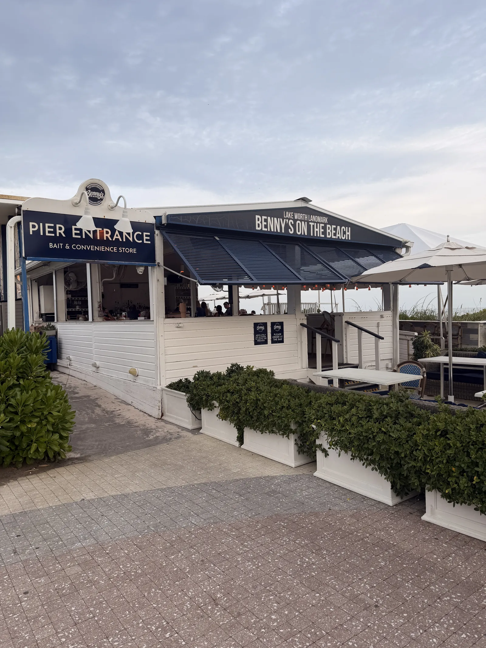 Pier Entrance and Benny's on the Beach signs on the white building, planters along the seating