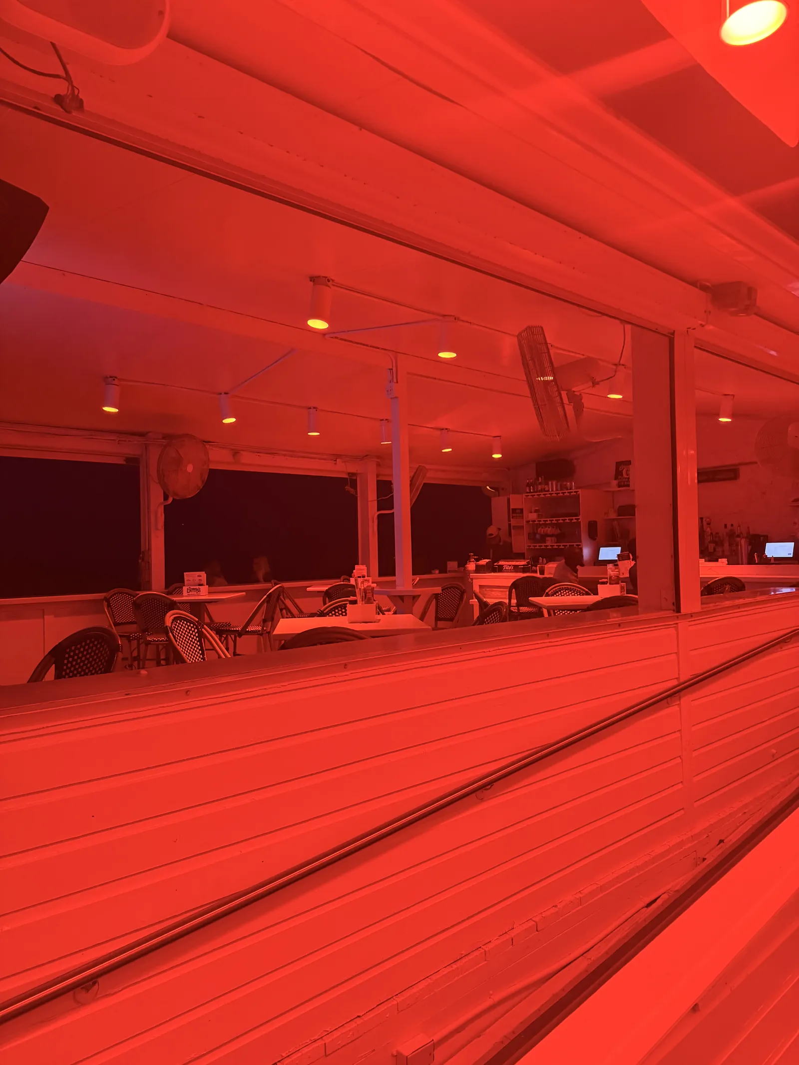 The dining room at Benny's under red lighting, empty tables and the bar at the back