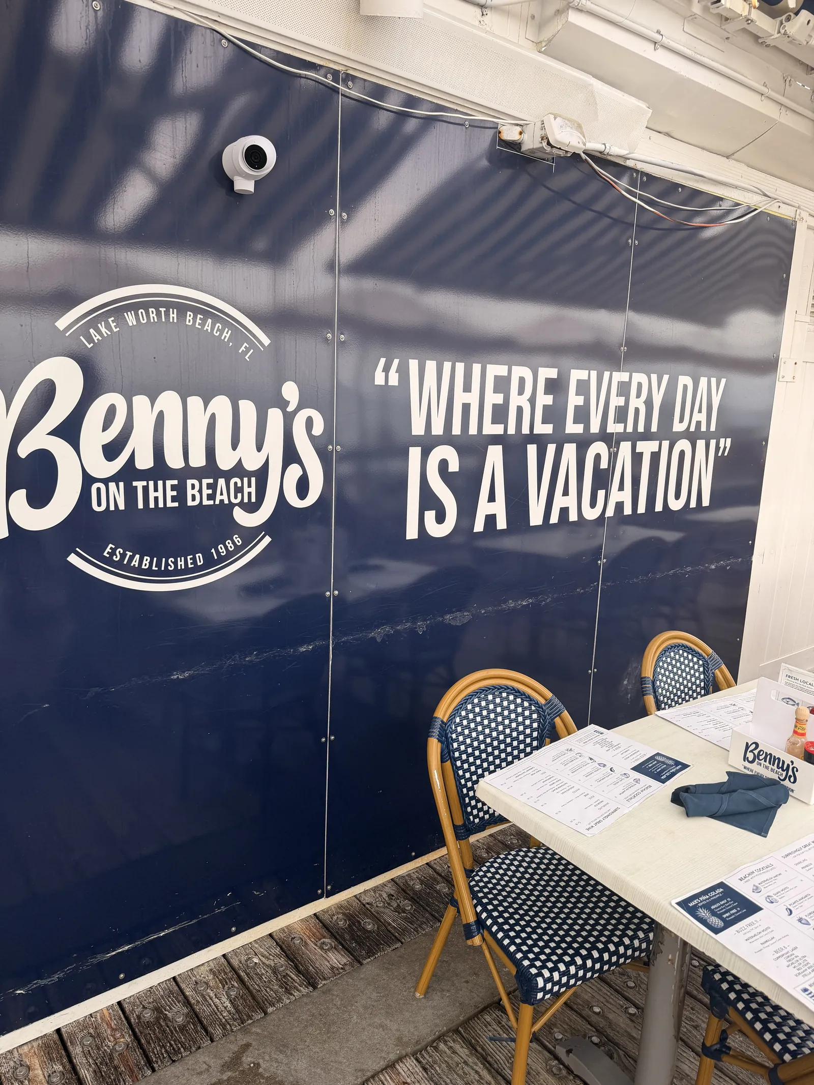 The Where Every Day Is A Vacation slogan on the blue wall at Benny's, a table set below it