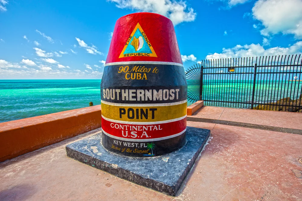 A colorful concrete buoy marks the Southernmost Point in the continental USA in Key West, Florida, with turquoise ocean water and a clear blue sky in the background.