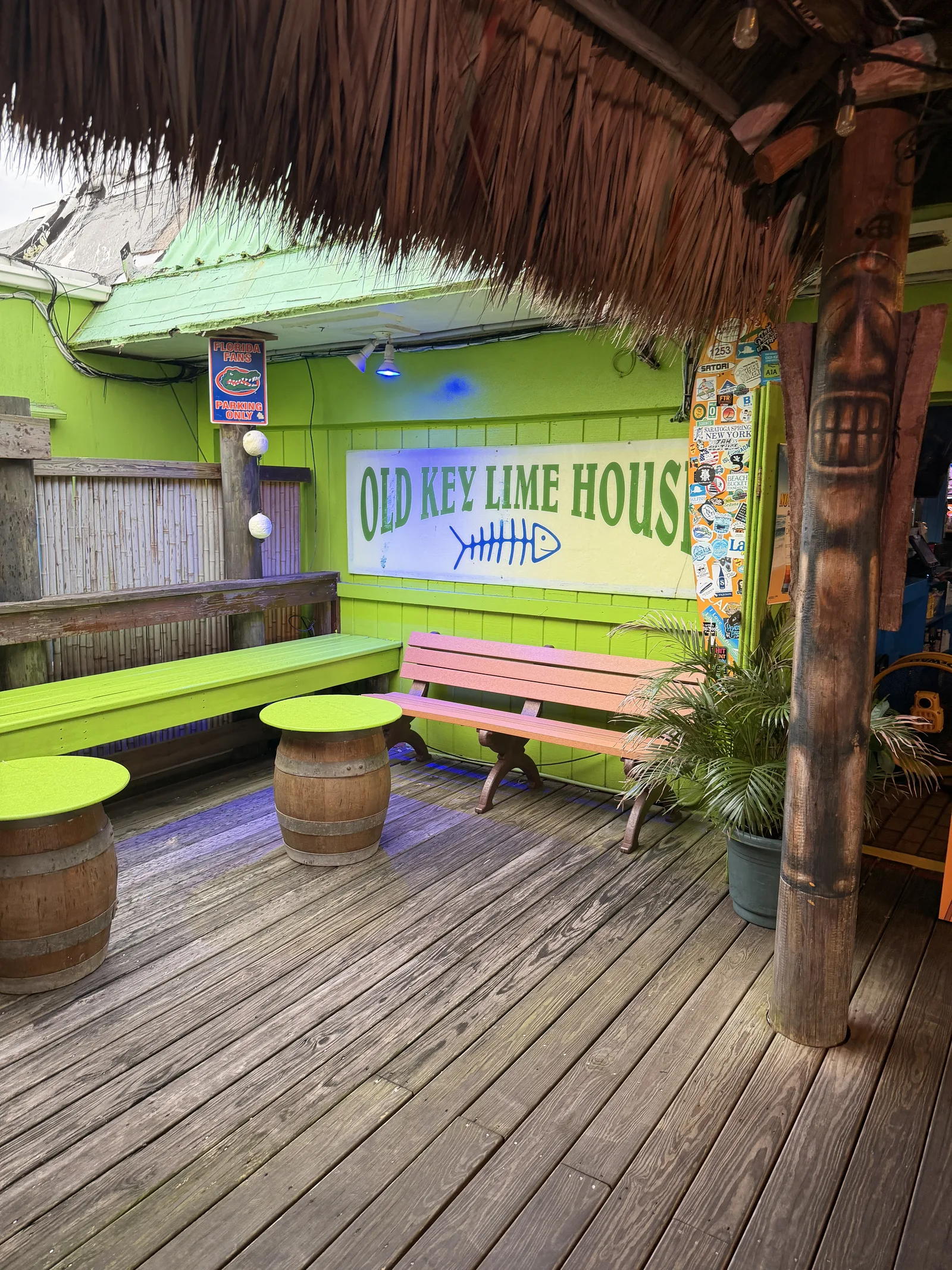 Barrel picnic tables and a pink bench under the thatched roof, the Old Key Lime House sign behind