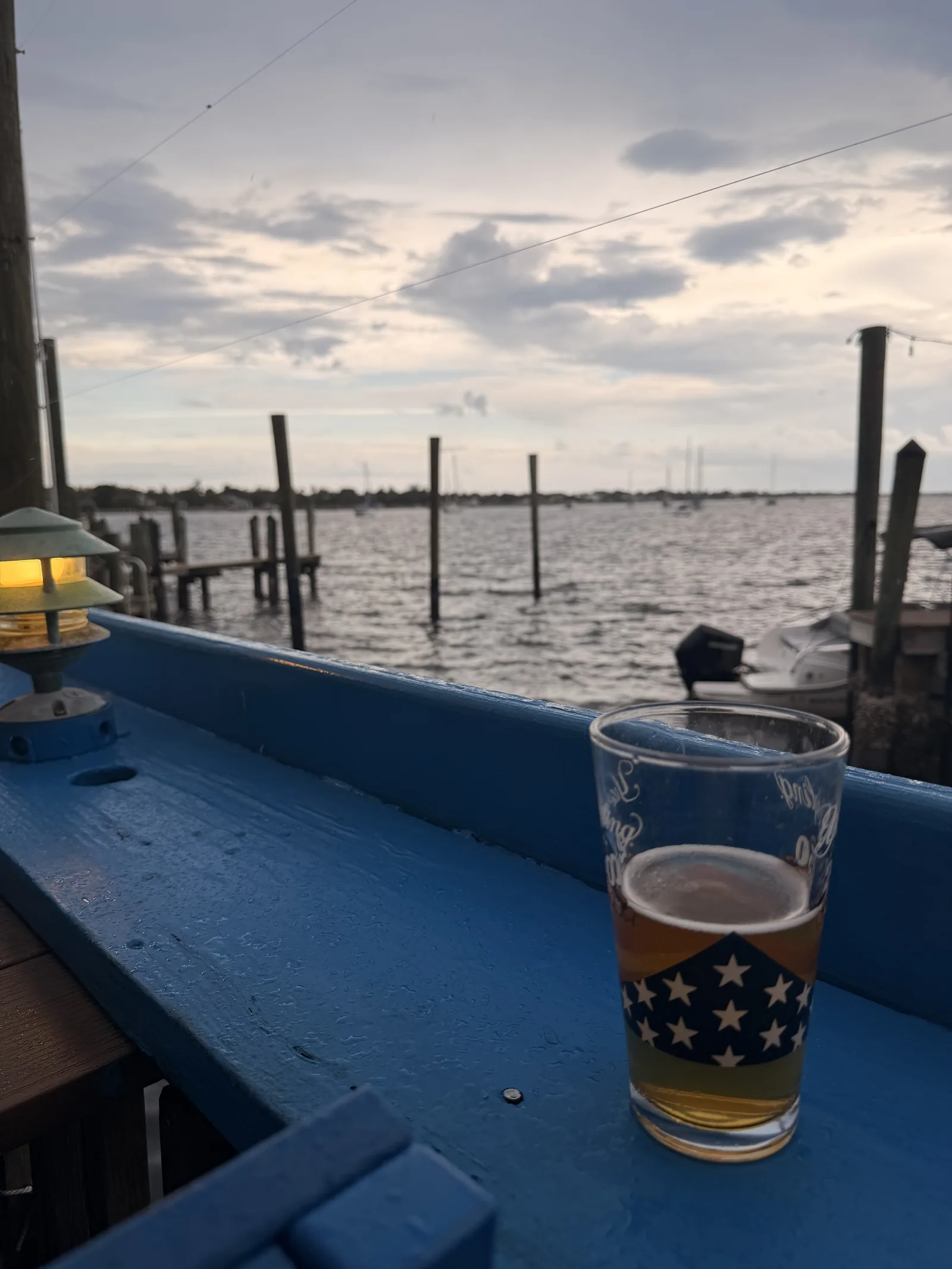 A pint glass on the blue railing at Old Key Lime House, boats and docks in the marina at sunset