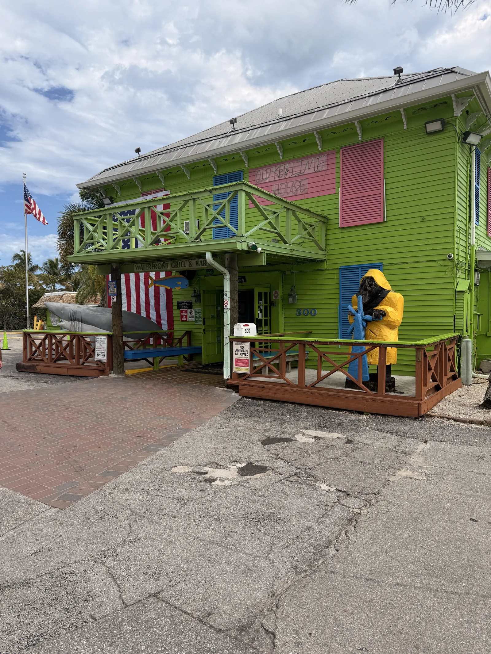 The green exterior of Old Key Lime House with pink shutters and a raincoated fisherman statue