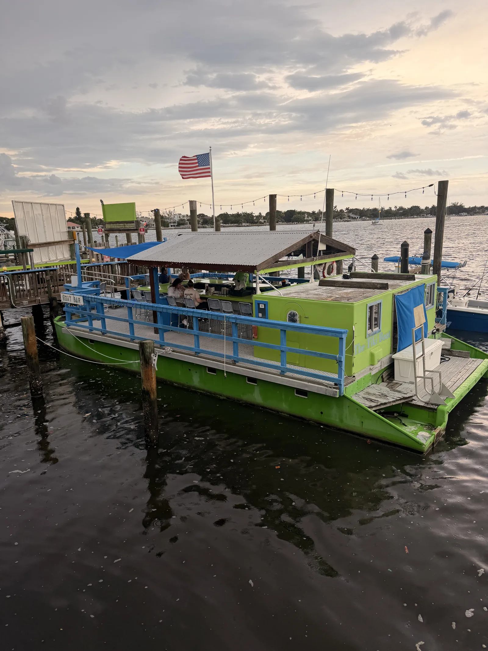 The green houseboat docked at Old Key Lime House, flag flying and string lights strung above