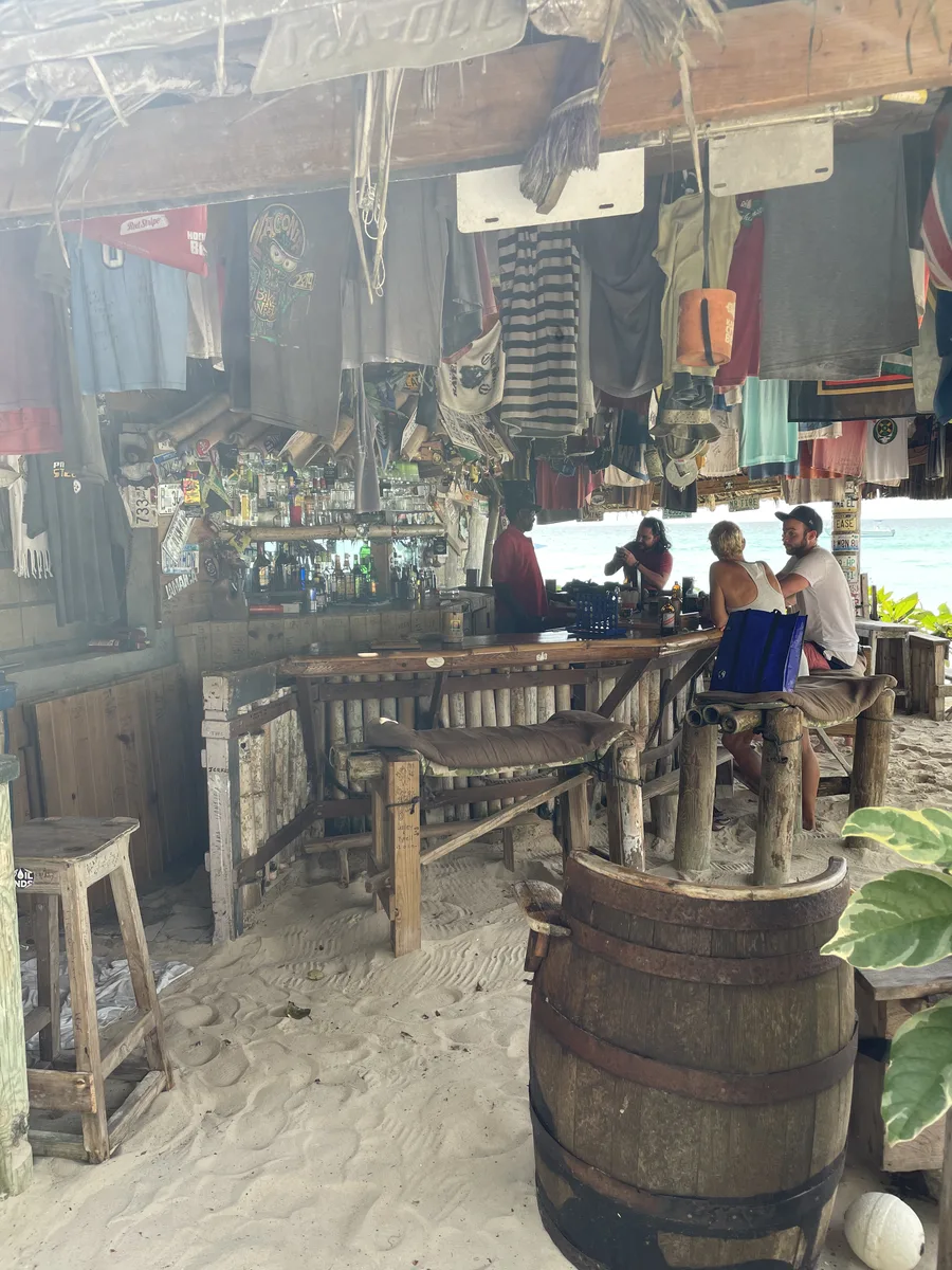 The bar at Tony's Hut with wooden stools standing in the sand and a whiskey barrel table