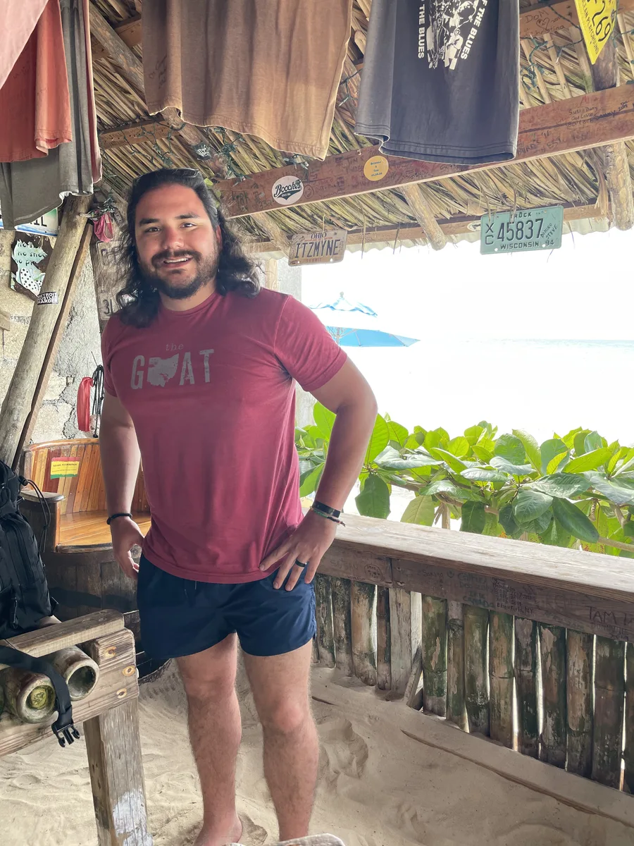 A guest at the rail of Tony's Hut beneath rafters hung with T-shirts and license plates