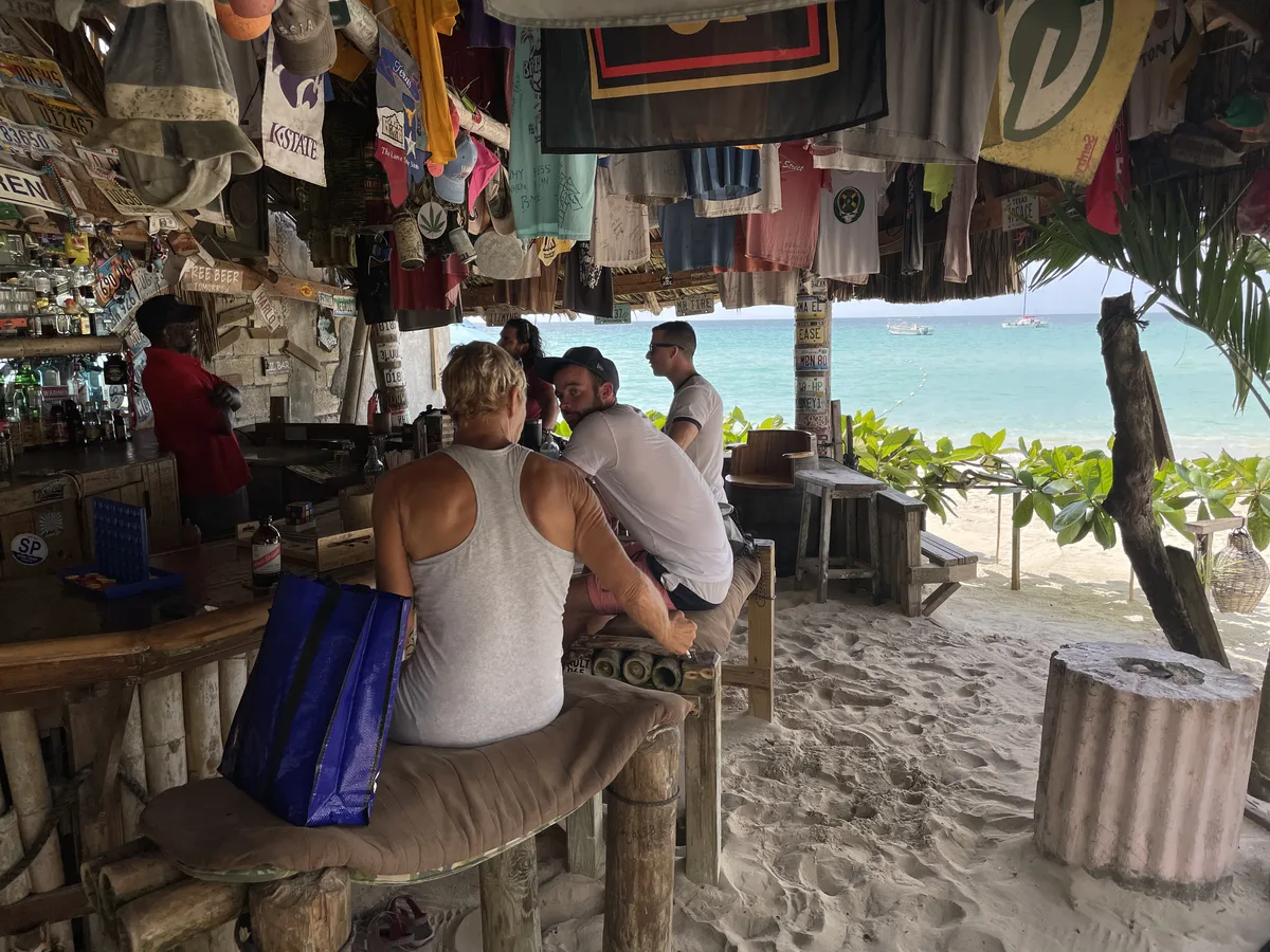 Inside Tony's Hut, bamboo bar and sand floor looking out to turquoise water and moored boats