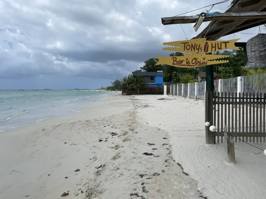 Hand-painted yellow arrow signs reading Tony's Hut and Bar is Open on the sand of Negril's Seven Mile Beach