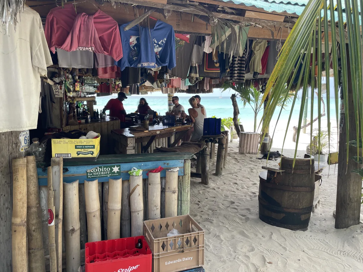 Red Stripe crates stacked beside the bamboo bar at Tony's Hut, sand underfoot throughout