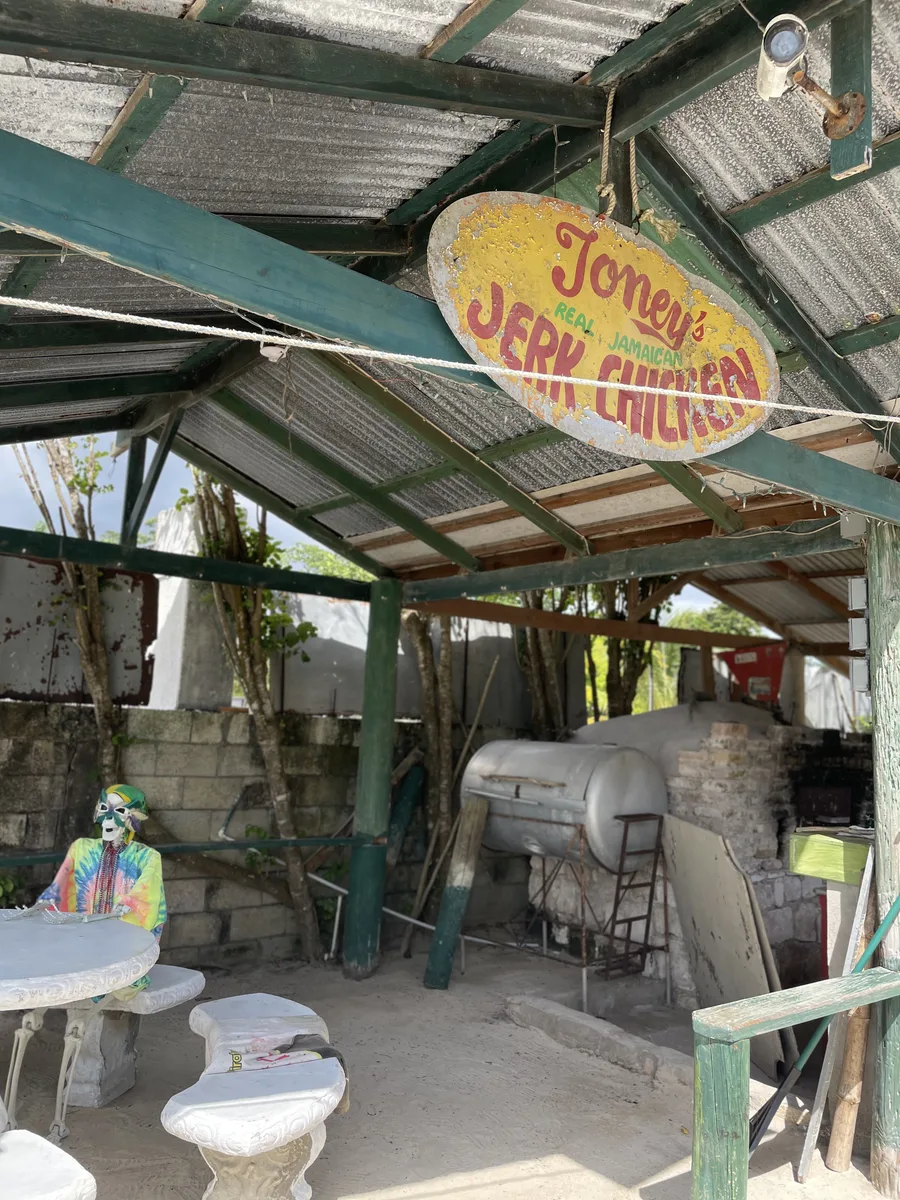 Toney's Real Jamaican Jerk Chicken sign above an oil-drum smoker behind Tony's Hut
